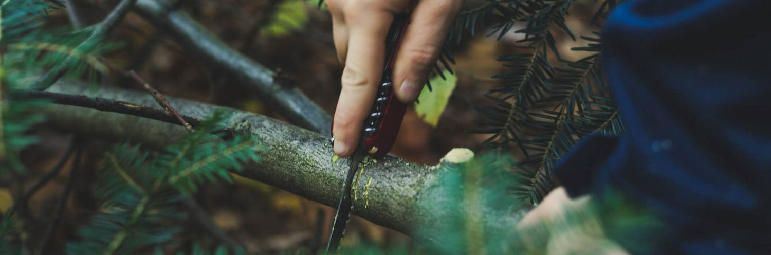 a man using a swiss army knife to cut a branch